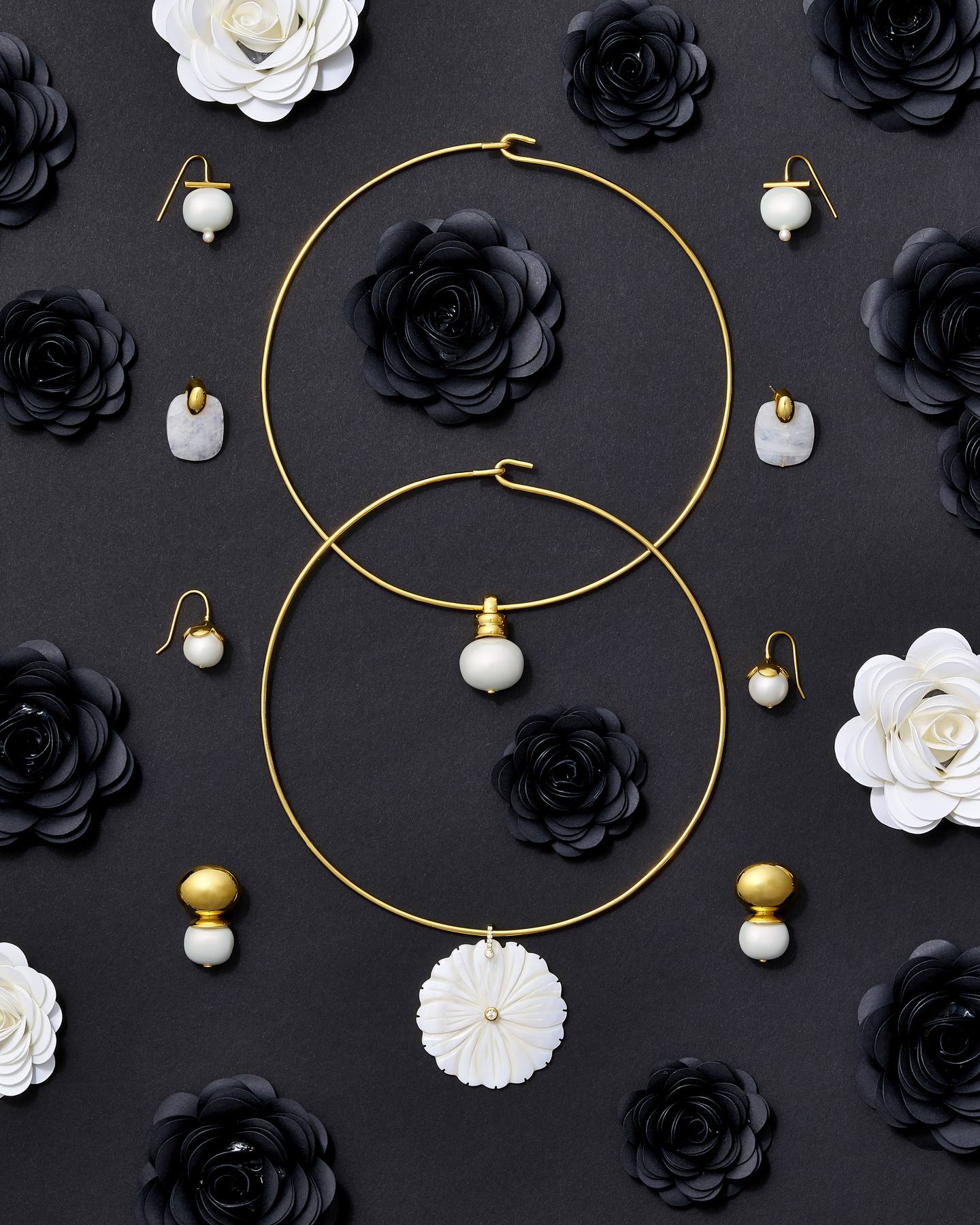 Pebble Pearl earrings and gold hoop necklaces arranged among black and white paper roses